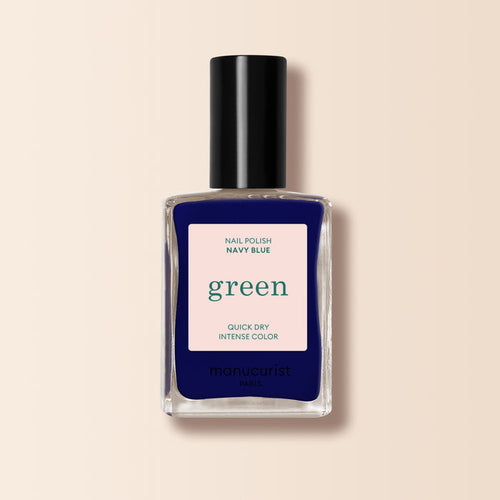 A bottle of Manucurist Navy Blue nail polish from the Green range with a black cap. The label says Nail Polish Navy Blue, Quick Dry Intense Color, and manucurist Paris. The background is soft beige.