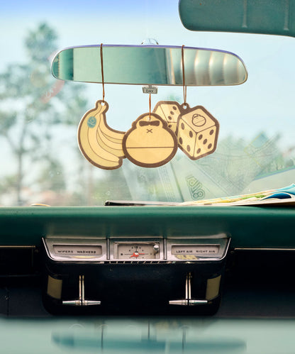Three Sun Bum Banana Air Freshener scents hanging from a car rearview mirror inside a vintage car.