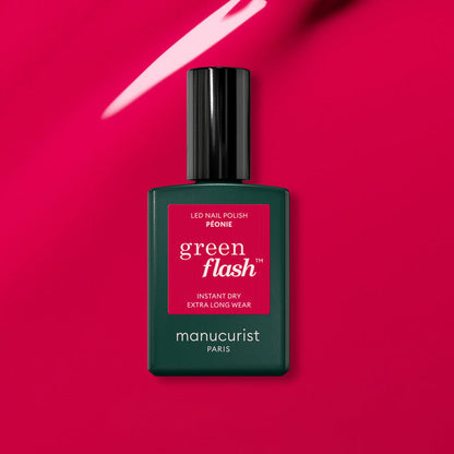 A bottle of Manucurist Péonie Green Flash gel polish rests on a glossy, bright pink surface reflecting light.