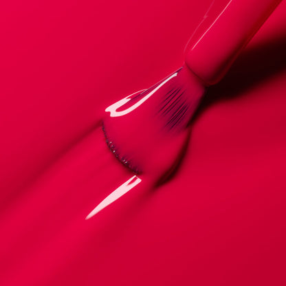 A close-up of a brush applying Manucurist’s Péonie gel polish in raspberry pink, creating smooth, glossy, vibrant strokes.