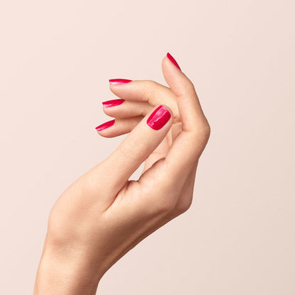 A close-up of neatly manicured nails painted in Péonie by Manucurist, a glossy raspberry pink gel polish, with the hand posed gracefully against a soft beige background.