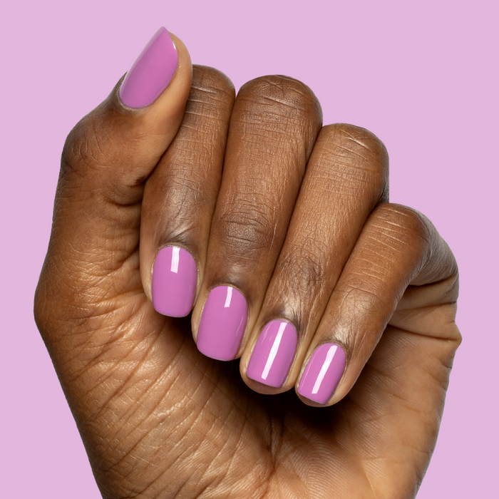 Hand with nails painted in bright floral purple pink shade using Petal - Gel polish on soft purple background