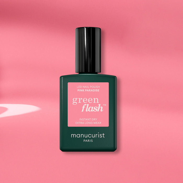 A Manucurist Pink Paradise Green Flash gel polish bottle, with a dark green base and black cap, is displayed on a pink background with soft shadows.