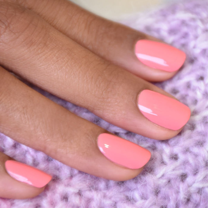 A close-up of a hand with neatly manicured nails painted in Manucurist’s Pink Paradise gel polish, resting on soft purple knit fabric.