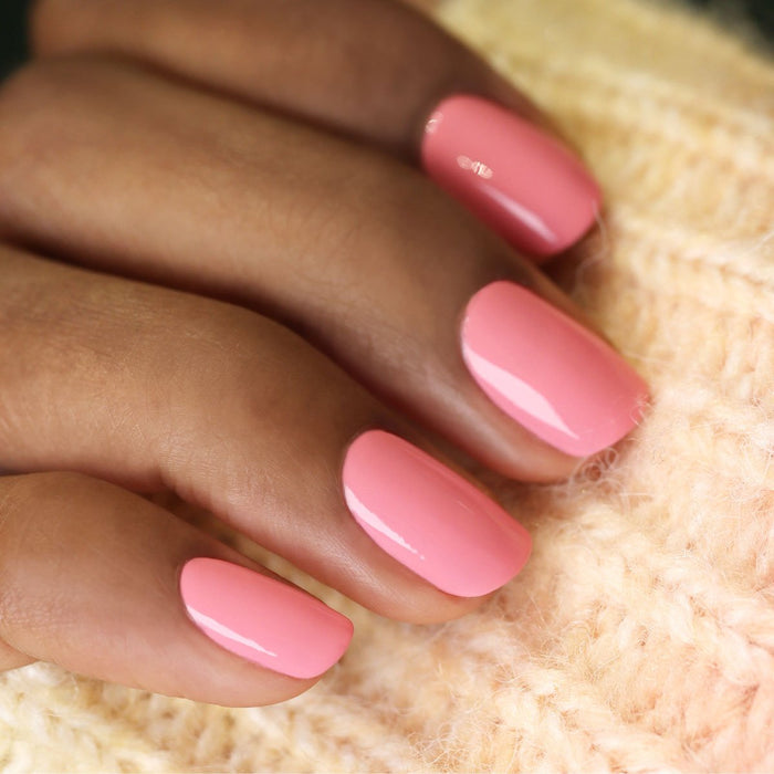 A close-up of a hand with neatly manicured nails painted in Manucurist’s Pink Paradise gel polish, resting on cream-colored knitted fabric.