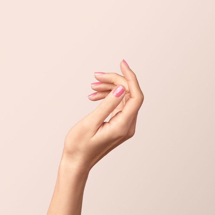 A hand with light skin is elegantly posed against a soft beige background, nails neatly manicured and coated in Manucurist’s Pink Paradise glossy candy pink gel polish.