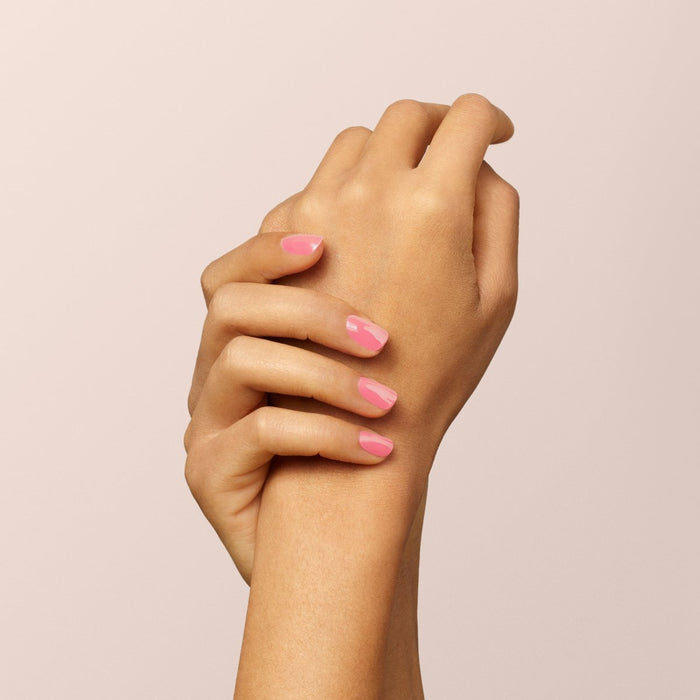 Two hands with light brown skin are clasped together against a pale pink background, nails neatly manicured and painted with Manucurist's Pink Paradise glossy gel polish.