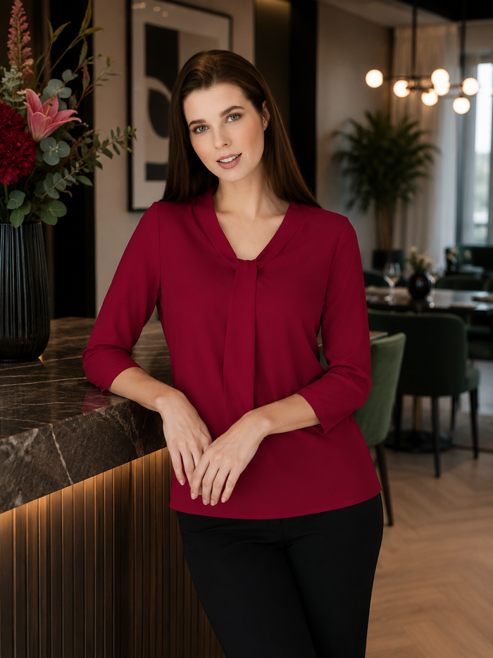 Woman in a red blouse standing in a modern indoor setting with decor elements.