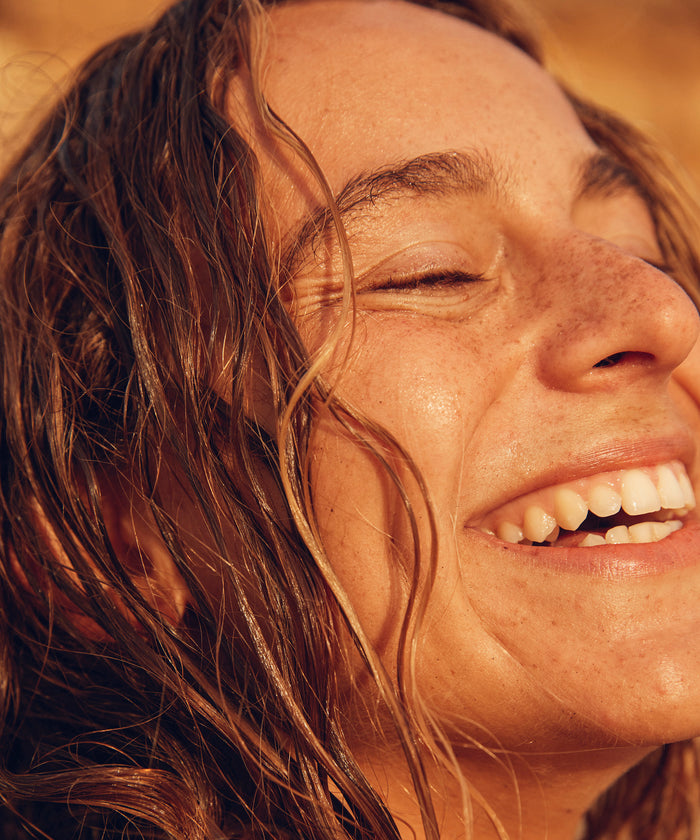 Close-up of a person with eyes closed, smiling outdoors.
