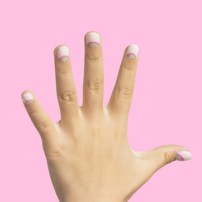 Rainbow Connection - Pressies | Extra Short Short | Round showing pastel pink press on nails with tiny rainbow designs on hand against pink background