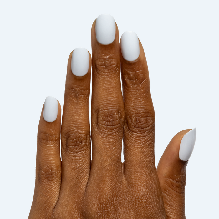 Rink | Short | Round - Tab Press-On matte white false nails on hand with smooth finish against pale background