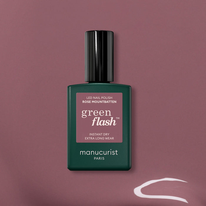 A bottle of Manucurist Rose Mountbatten gel polish stands upright on a mauve background, with a white curved streak in the bottom right corner.