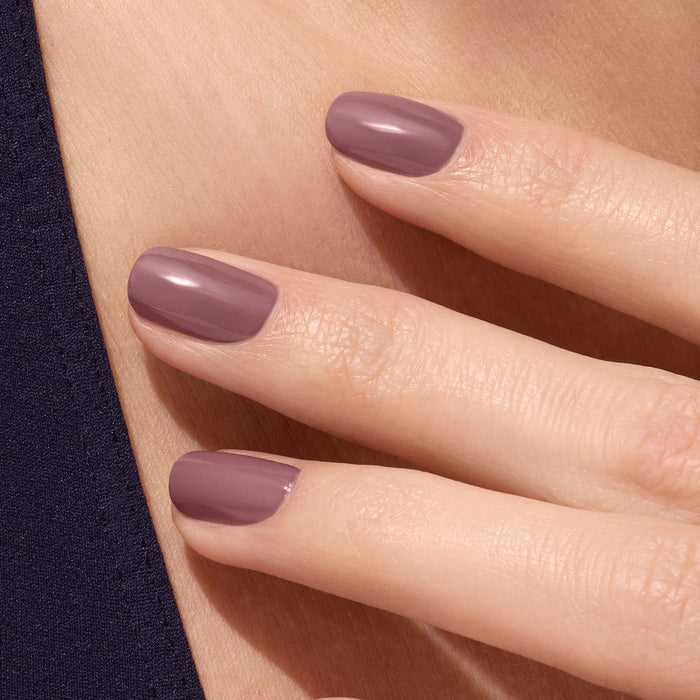 A close-up of a hand with neatly manicured nails painted in Manucurist's Rose Mountbatten, a glossy pinky taupe gel polish, resting gently on skin beside dark fabric.