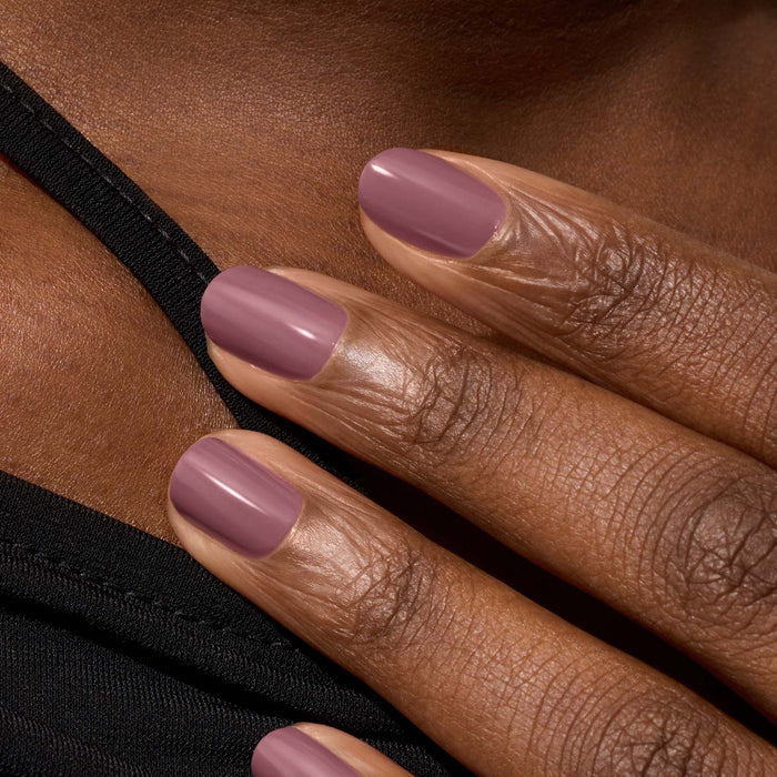 A close-up of a hand with medium brown skin, featuring neatly manicured nails painted in Manucurist's Rose Mountbatten gel polish, resting gently on a shoulder clad in black.
