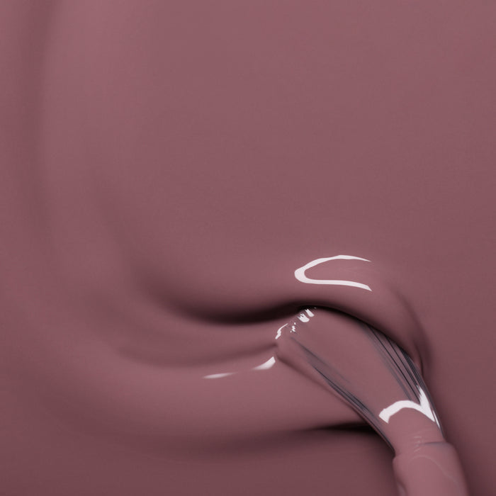 A close-up of a brush applying smooth Manucurist Rose Mountbatten nail polish, creating glossy, flowing streaks of camouflage pink.