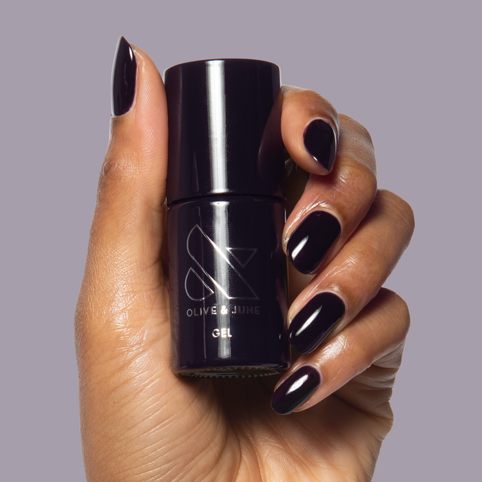 SD - Gel bottle held with matching deep plum gel polish on almond-shaped nails by Olive and June