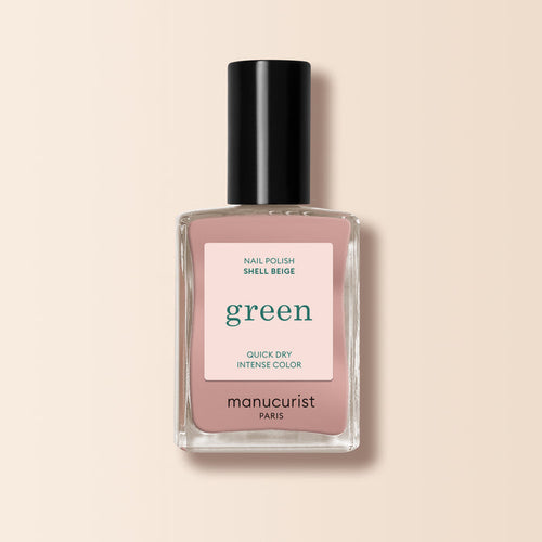 A bottle of Manucurist Shell Beige nail polish from the Green™ range, with a black cap, clear glass bottle, and a beige-pink label reading “green, quick dry intense color,” set against a light beige background.