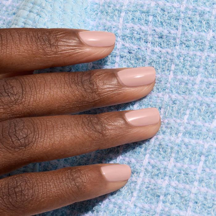 A hand with short, neatly manicured nails painted in Manucurist's Shell Beige nail polish rests on a light blue textured fabric.