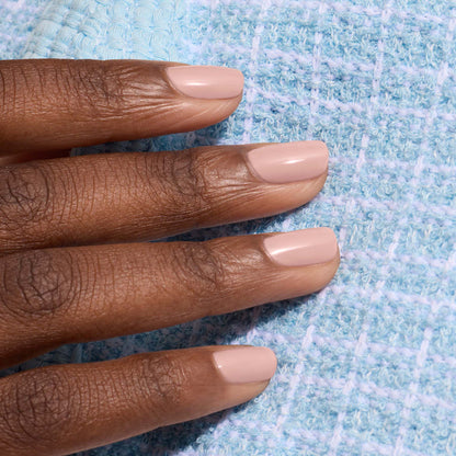 A hand with short, neatly manicured nails painted in Manucurist's Shell Beige nail polish rests on a light blue textured fabric.
