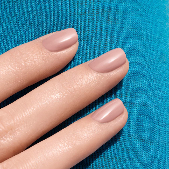 Three neatly manicured fingers showcase Manucurist's Shell Beige nail polish, resting on bright blue textured fabric.