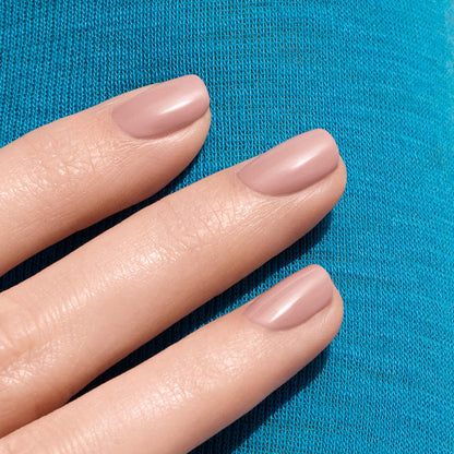 Three neatly manicured fingers showcase Manucurist's Shell Beige nail polish, resting on bright blue textured fabric.