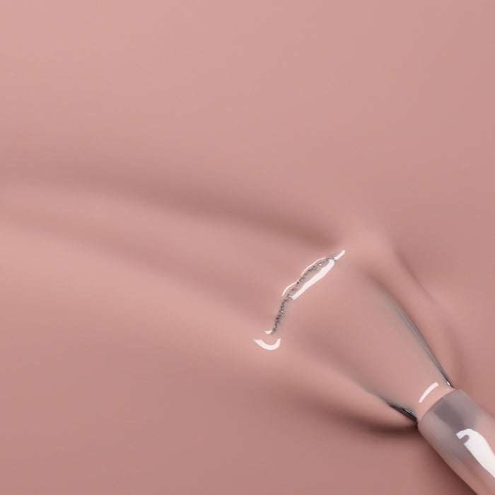 A close-up of a brush applying Manucurist's Shell Beige nail polish, revealing glossy streaks and the delicate pinkish beige texture on a smooth surface.