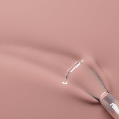 A close-up of a brush applying Manucurist's Shell Beige nail polish, revealing glossy streaks and the delicate pinkish beige texture on a smooth surface.