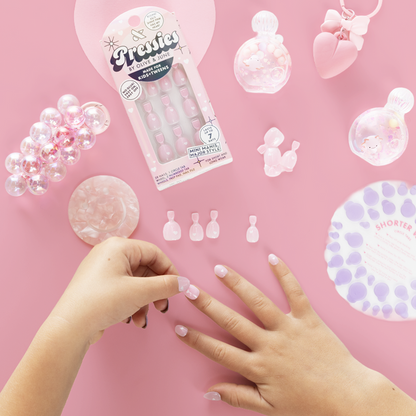 Shiny Pink Has My Heart - Pressies | Extra Short Short | Round showing hands applying soft pink false nails on pink surface with mani tools