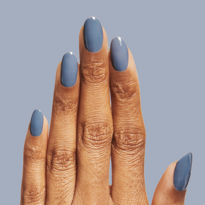 Fingers with nails coated in Slate - Gel, a smooth midtone slate blue gel polish on a muted blue background