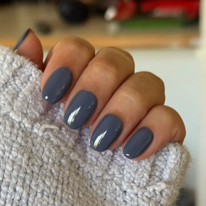 Close-up of hand with glossy Slate - Gel polish manicure on rounded nails, resting on textured light gray fabric