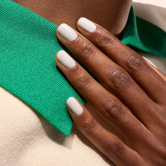 A hand with neatly manicured, short nails coated in Manucurist's Snow pure white nail polish rests on a green collar of a cream-colored garment.