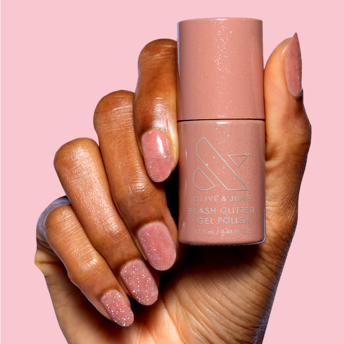 Hand holding Sparkly Pink Drink Gel polish bottle showing glittery blush pink gel manicure nails on soft pink background