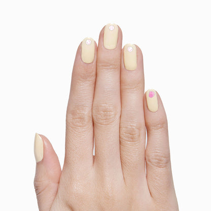 Hand with pale yellow polish featuring Sports Pack nail stickers of tennis balls and basketball for a playful mani