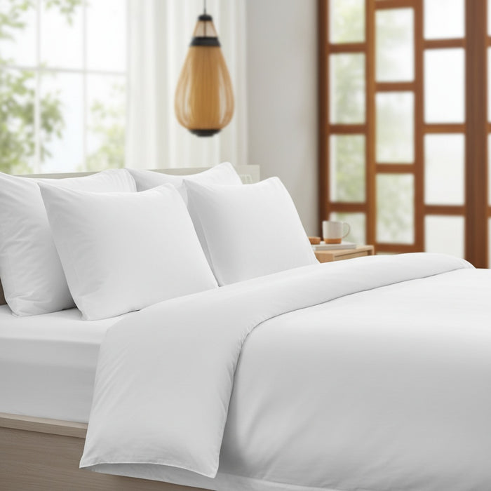 White bedding set on a bed in a bright bedroom with large windows.