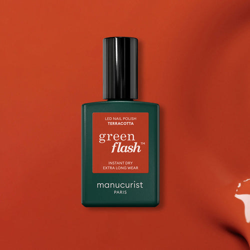 A bottle of Manucurist’s Terracotta gel polish is shown against a red earth–inspired background. The rectangular bottle has a dark green body with a sleek black cap, highlighting the rich Terracotta shade.