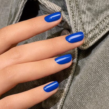 A hand with neatly manicured nails painted in Manucurist’s Ultramarine electric blue nail polish rests against a light gray denim jacket.